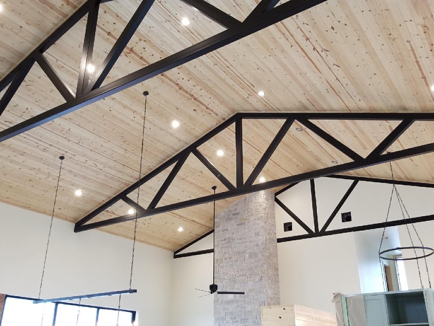 Barndominium interior with black steel trusses, pine tongue-and-groove ceiling, and brick fireplace column — Tincher's