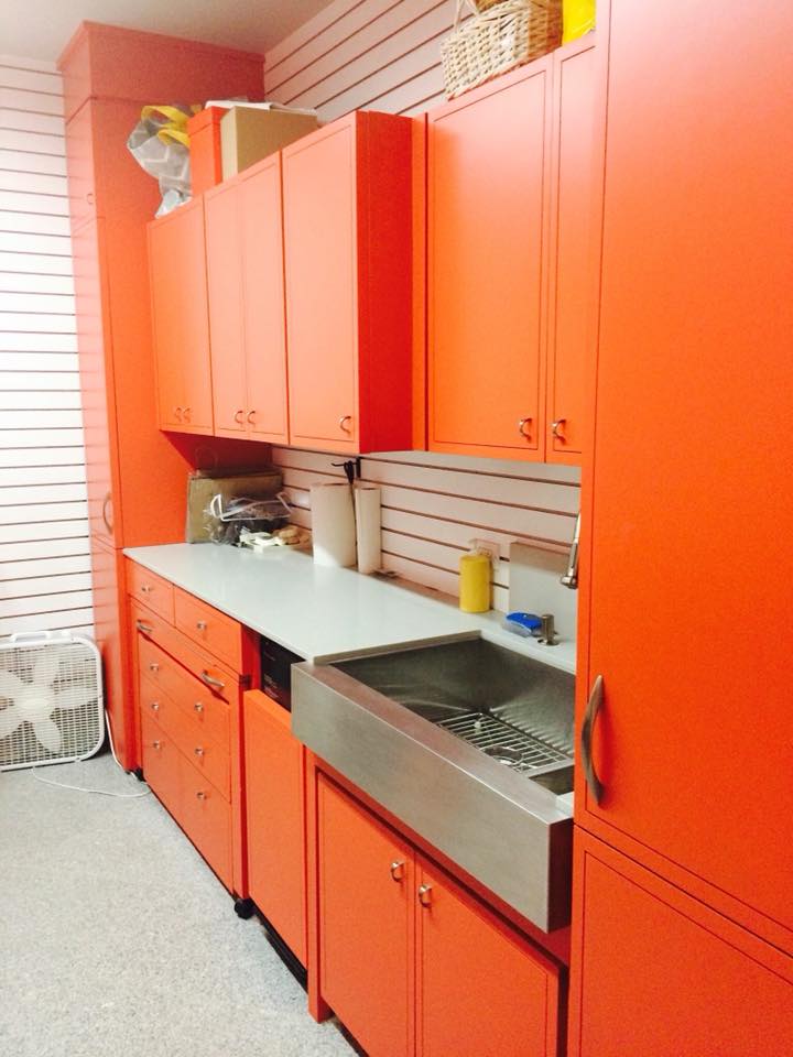 Custom laundry room cabinetry in bold orange with stainless farmhouse sink, built-in drawers, and full-height storage — Tincher's Custom Homes