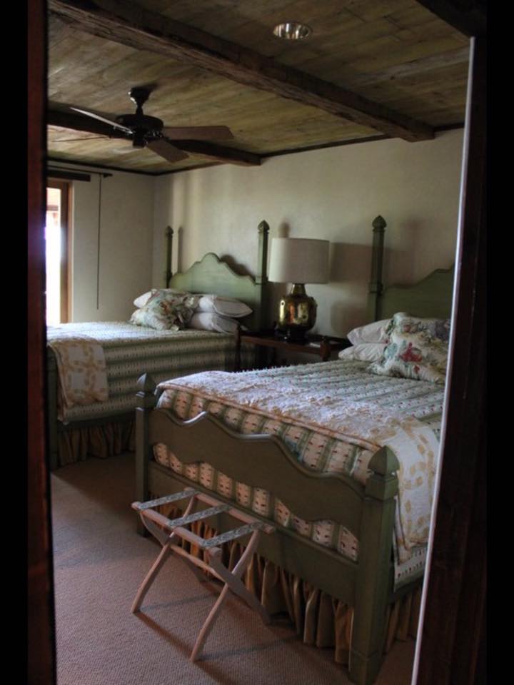 Guest bedroom with green painted four-poster beds, cedar plank ceiling with beams, and ceiling fan — custom home interior by Tincher's
